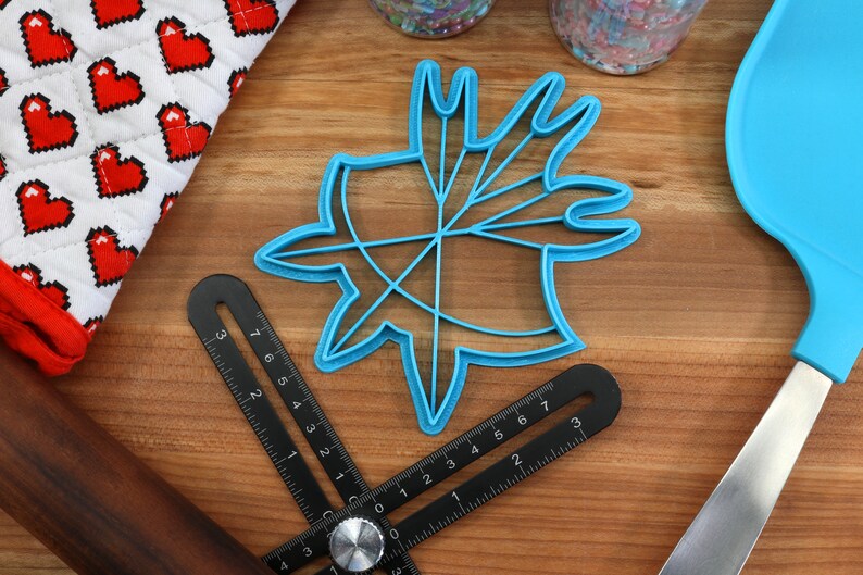 May include: A blue plastic cookie cutter shaped like a starburst with multiple points. The cutter is on a wooden surface with a ruler and a rolling pin.