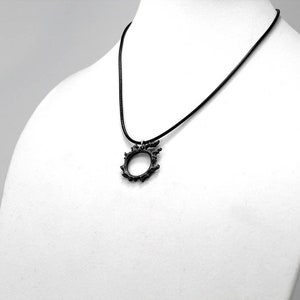 Puede incluir: Un collar negro con un colgante circular que presenta un dise&ntilde;o puntiagudo e intrincado.