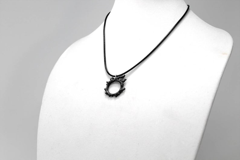 Puede incluir: Un collar negro con un colgante circular que presenta un dise&ntilde;o puntiagudo e intrincado.