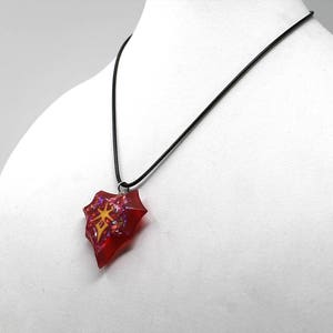 May include: A red and gold necklace with a heart-shaped pendant. The pendant is filled with glitter and has a gold design in the center.