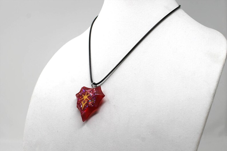 May include: A red and gold necklace with a heart-shaped pendant. The pendant is filled with glitter and has a gold design in the center.