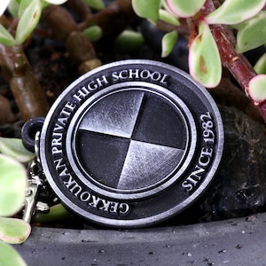 May include: A silver-colored metal keychain with the words "Gekkoukan Private High School Since 1982" around the edge. The center of the keychain features a four-quadrant design.