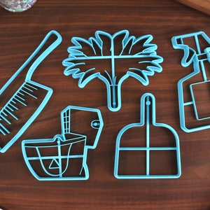 May include: A set of six blue plastic cookie cutters shaped like cleaning supplies. The cutters include a broom, dustpan, spray bottle, sponge, scrub brush, and a bucket.