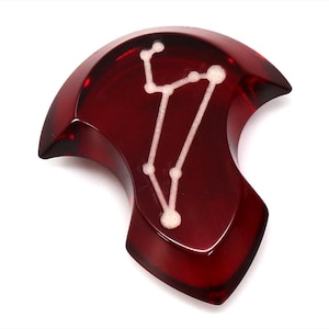 Op de afbeelding: Een rode, harsvormige dobbelsteen in de vorm van een sterrenbeeld met een wit sterrenbeeldontwerp.