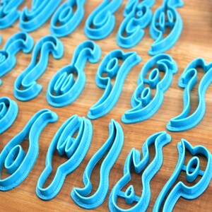 May include: A set of blue plastic cookie cutters shaped like different letters of the alphabet. The cutters are arranged in rows on a wooden surface.