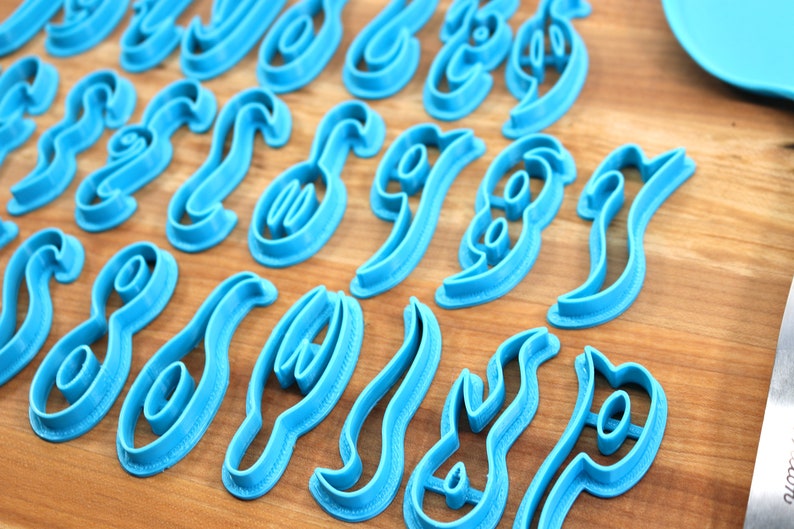 May include: A set of blue plastic cookie cutters shaped like different letters of the alphabet. The cutters are arranged in rows on a wooden surface.