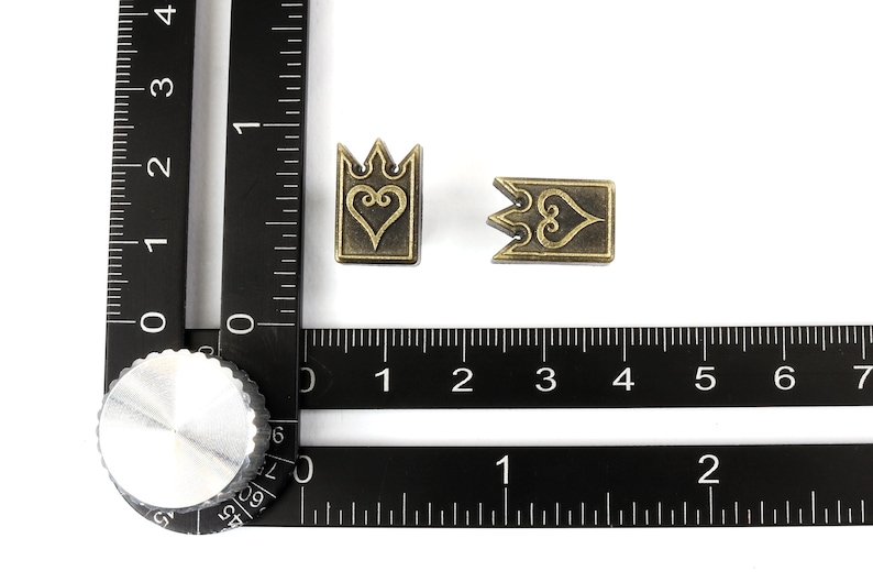 May include: Two antique brass-colored metal charms. One charm is a crown shape with a heart design, and the other is a rectangular shape with a heart design. The charms are approximately 0.5 inches in size.