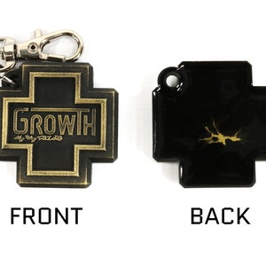 May include: A black leather keychain with a gold cross design. The front of the keychain features the word "GROWTH" in gold lettering. The back of the keychain has a gold splatter design.