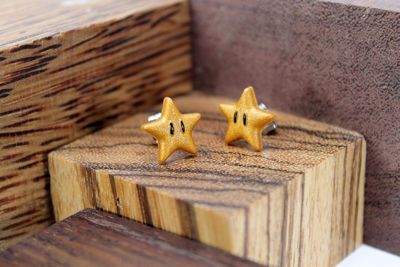 May include: A pair of gold star-shaped earrings with black accents. The earrings are on a wooden surface.
