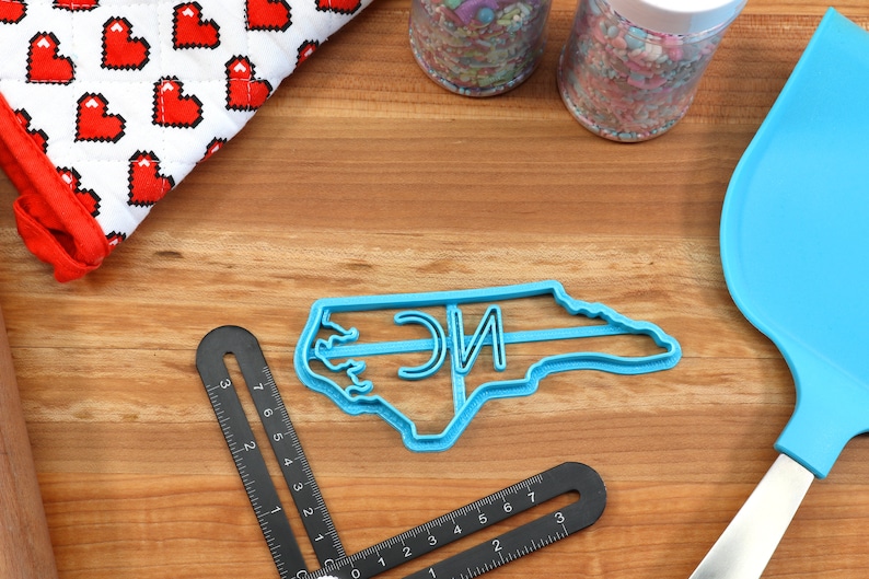 May include: Blue plastic cookie cutter shaped like the state of North Carolina with the letters "NC" inside.