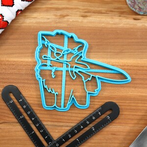 May include: A blue plastic cookie cutter shaped like a llama wearing a hat and holding a sword. The llama is facing the right side of the image.