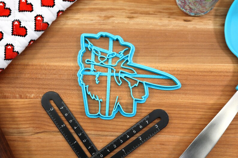 May include: A blue plastic cookie cutter shaped like a llama wearing a hat and holding a sword. The llama is facing the right side of the image.