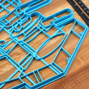 May include: A blue plastic cookie cutter shaped like a city skyline. The cutter is on a wooden surface.