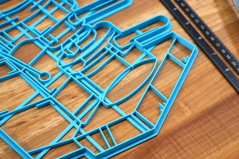 May include: A blue plastic cookie cutter shaped like a city skyline. The cutter is on a wooden surface.