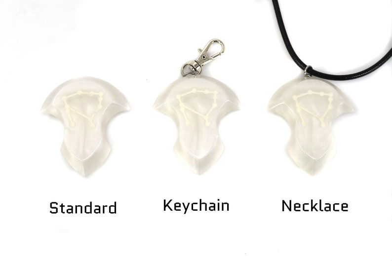 Op de afbeelding: Drie versies van een witte hanger met een sterrenbeeldontwerp. De hanger is verkrijgbaar als standaardstuk, sleutelhanger en ketting.