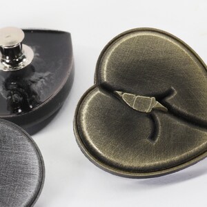 May include: Three heart-shaped metal buttons. One button is black with a silver stud, one is black with a crack, and one is gold with a crack.