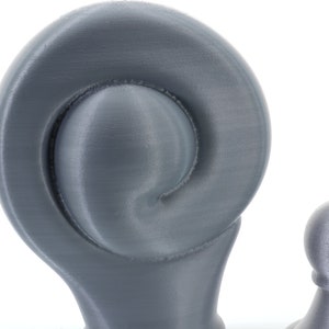 K&ouml;nnte beinhalten: Nahaufnahme von zwei grauen Dekorationsgegenst&auml;nden. Das gr&ouml;&szlig;ere Objekt hat ein spiralf&ouml;rmiges Design, w&auml;hrend das kleinere eine abgerundete Form hat. Beide Objekte haben eine strukturierte Oberfl&auml;che und sind vor einem wei&szlig;en Hintergrund platziert. Die Objekte scheinen 3D-gedruckt zu sein.
