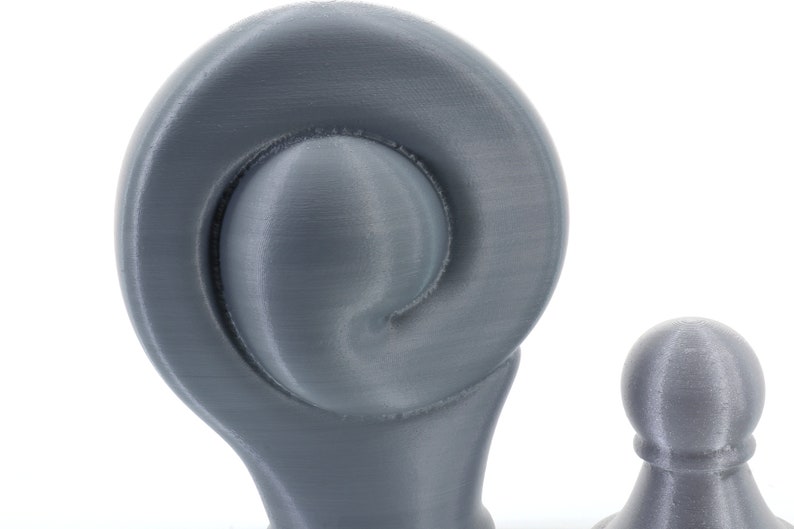 K&ouml;nnte beinhalten: Nahaufnahme von zwei grauen Dekorationsgegenst&auml;nden. Das gr&ouml;&szlig;ere Objekt hat ein spiralf&ouml;rmiges Design, w&auml;hrend das kleinere eine abgerundete Form hat. Beide Objekte haben eine strukturierte Oberfl&auml;che und sind vor einem wei&szlig;en Hintergrund platziert. Die Objekte scheinen 3D-gedruckt zu sein.