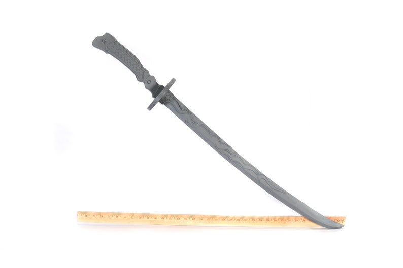 Może przedstawiać: Szary miecz katana z teksturowanym uchwytem i wzorem ostrza. Miecz ma około 76 cm długości. Drewniana linijka jest umieszczona obok miecza dla skali, na białym tle.