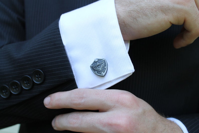 May include: A pair of silver cufflinks featuring a stylised shield with a winged eye design.