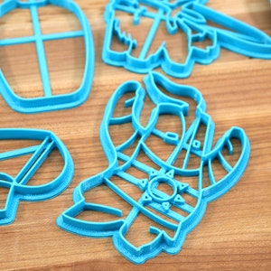 May include: A set of blue plastic cookie cutters shaped like a llama, a cactus, and a bottle. The cutters are on a wooden surface.
