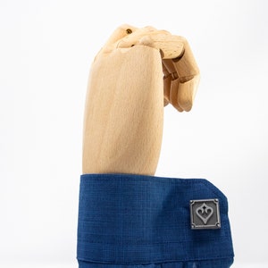 May include: A pair of silver cufflinks with a heart design. The cufflinks are on a blue shirt cuff.