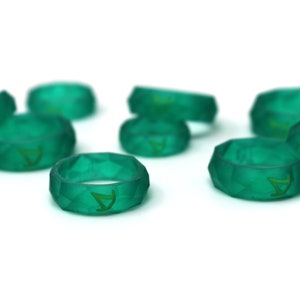 Pu&ograve; includere: Un gruppo di otto anelli in silicone verde acqua con un design geometrico. Ogni anello ha una lettera 'A' dorata incisa all'interno.