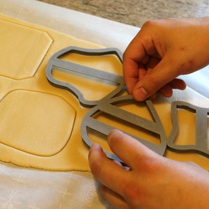 May include: A person using a gray cookie cutter shaped like a bee to cut out shapes from a sheet of cookie dough.