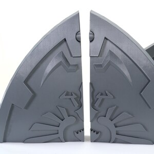 May include: Two gray, 3D printed, half-circle bookends with a stylized design. The bookends are separated and show a detailed, intricate design.