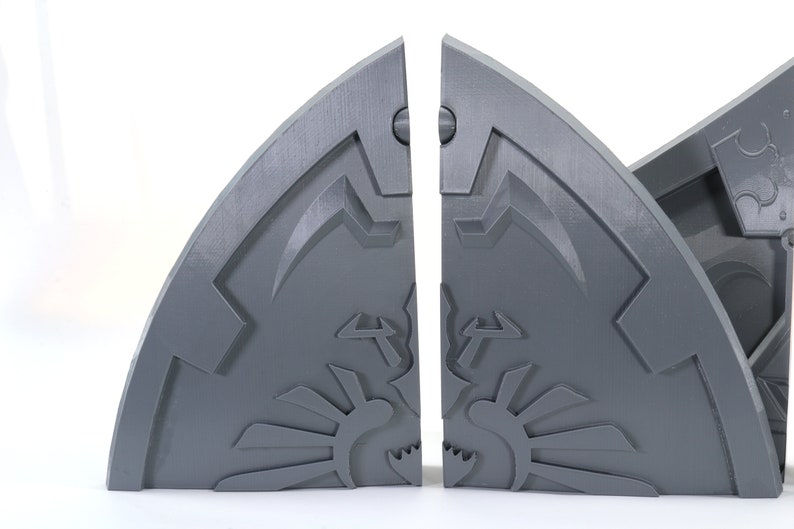 May include: Two gray, 3D printed, half-circle bookends with a stylized design. The bookends are separated and show a detailed, intricate design.