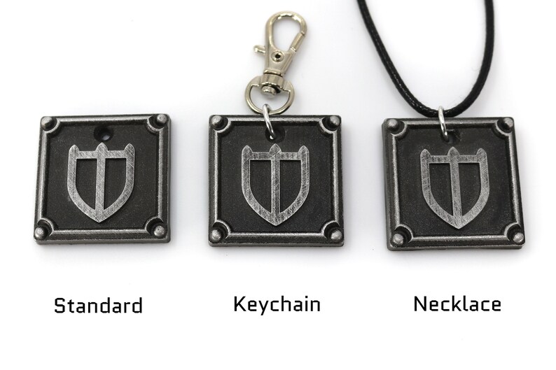 May include: Three silver-coloured metal pendants featuring a shield design. The pendants are displayed in three different styles: standard, keychain, and necklace.