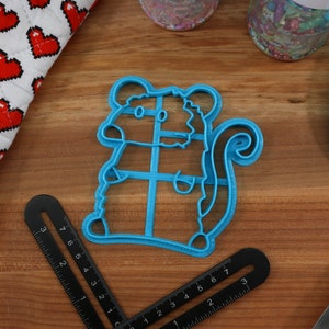 May include: A blue plastic cookie cutter shaped like a squirrel. The cutter has a detailed design with a bushy tail and a small body.