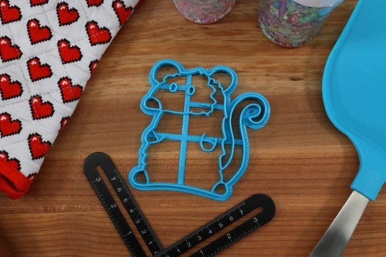 May include: A blue plastic cookie cutter shaped like a squirrel. The cutter has a detailed design with a bushy tail and a small body.