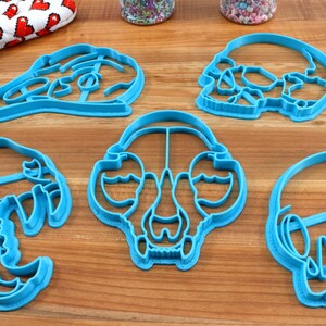 May include: Five blue plastic cookie cutters shaped like different animal skulls. The cutters are on a wooden surface.