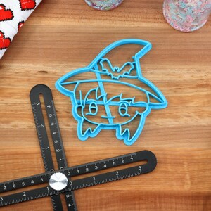 May include: A blue plastic cookie cutter shaped like a witch with a hat and a bat on the hat.
