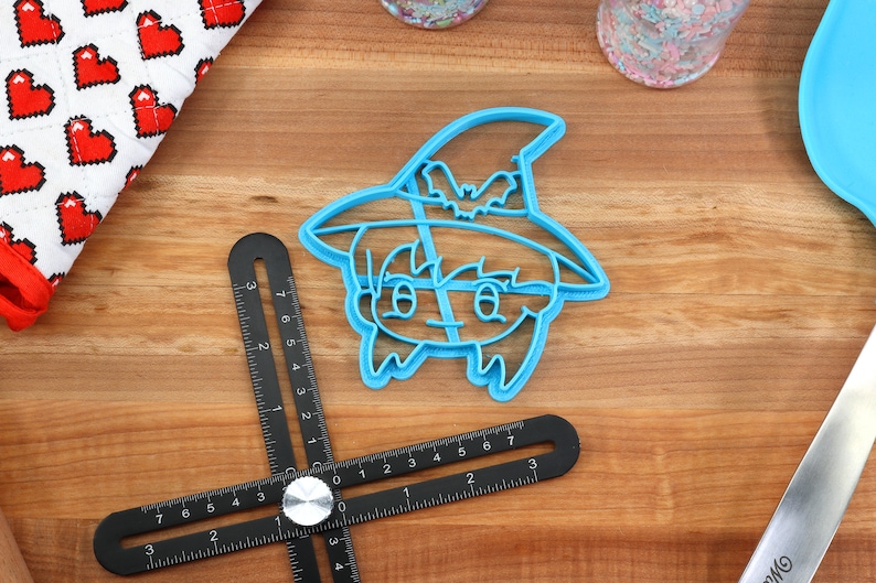 May include: A blue plastic cookie cutter shaped like a witch with a hat and a bat on the hat.