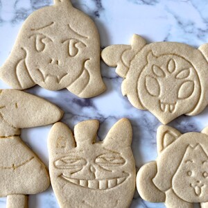 May include: Five decorated sugar cookies, each featuring a different character from the video game "Undertale". The cookies are light brown and have detailed designs.