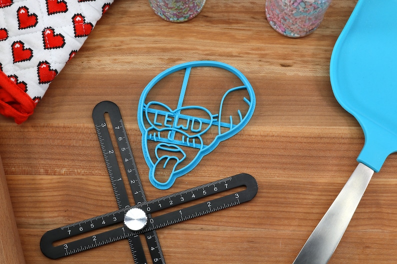 Puede incluir: Cortador de galletas de pl&aacute;stico azul con forma de cara de dibujos animados con la palabra "LELJD" escrita sobre los ojos.