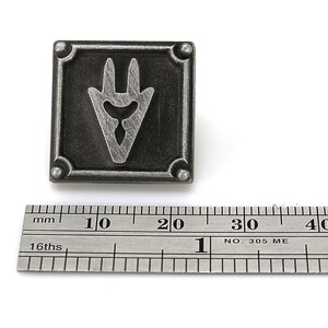 May include: A silver-toned metal pin with a stylized, three-pronged symbol in a square frame. The pin measures approximately 2 cm in width.