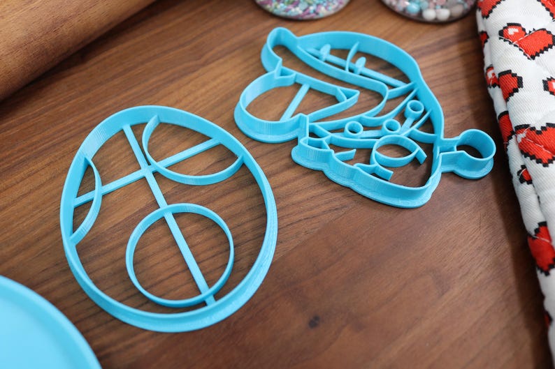 Op de afbeelding: Twee blauwe plastic koekjesvormen, een in de vorm van een cirkel met een ontwerp van overlappende cirkels en de andere in de vorm van een gestileerde bloem met een kleine cirkel aan het einde van een stengel.