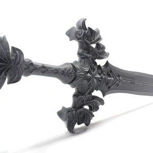 May include: A gray, intricately detailed sword with a pointed tip and a decorative hilt. The sword has a floral design and a sharp blade.