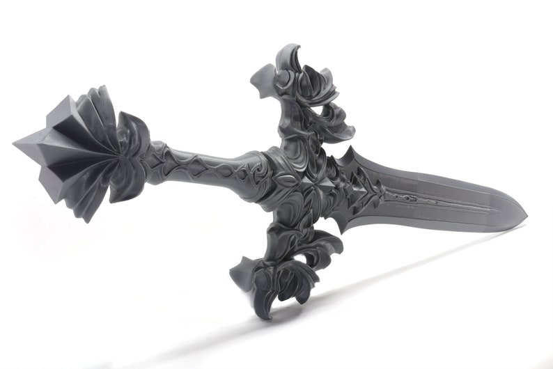 May include: A gray, intricately detailed sword with a pointed tip and a decorative hilt. The sword has a floral design and a sharp blade.