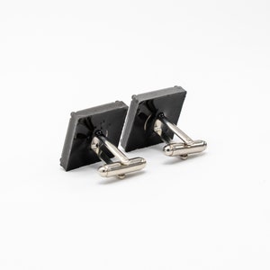 May include: A pair of silver cufflinks with black square-shaped fronts.