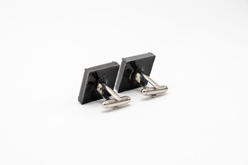 May include: A pair of silver cufflinks with black square-shaped fronts.