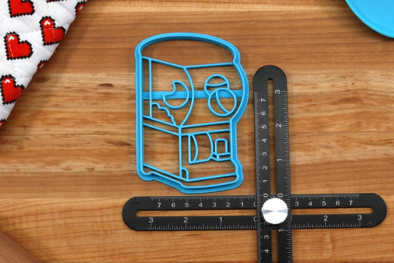 May include: Blue plastic cookie cutter shaped like a gumball machine with a clear window and a coin slot. The cutter is about 3 inches tall.