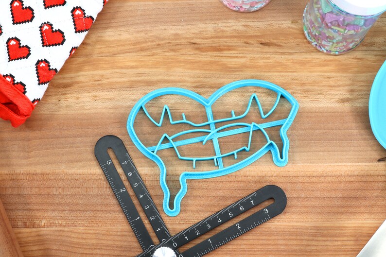 May include: A blue plastic cookie cutter shaped like a dripping heart. The cutter has a detailed design with multiple lines and curves.