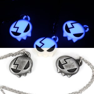 May include: Two silver necklaces with a glow-in-the-dark pendant shaped like a ghost with a lightning bolt design. The pendant is silver and black with a black lightning bolt. The necklaces are on a white background.