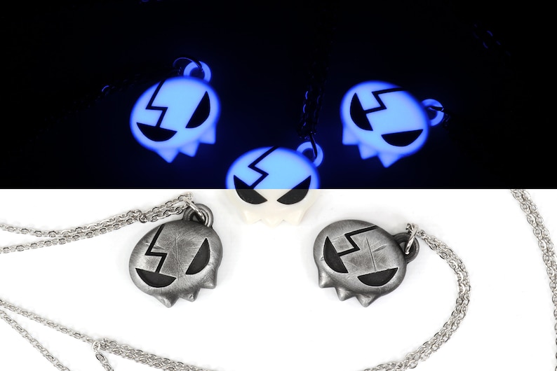 May include: Two silver necklaces with a glow-in-the-dark pendant shaped like a ghost with a lightning bolt design. The pendant is silver and black with a black lightning bolt. The necklaces are on a white background.