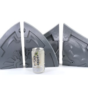 May include: Four gray 3D printed pieces of a puzzle, resembling a shield with intricate details. A can of Japanese beer is in the center.