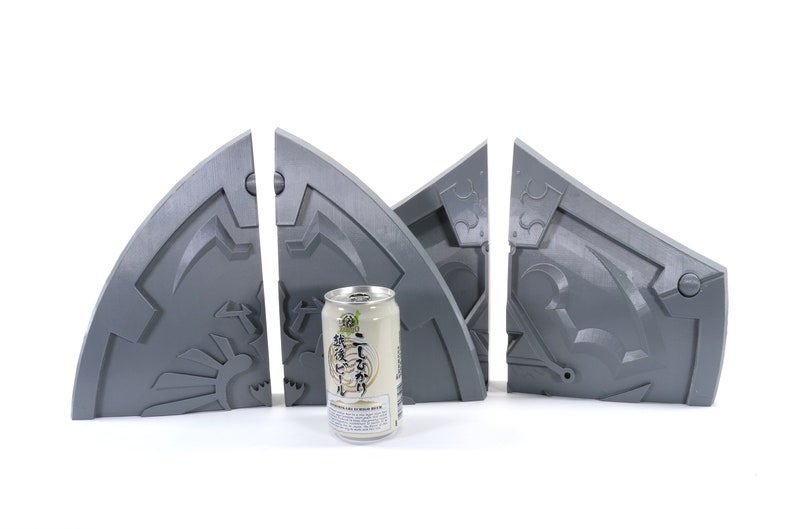May include: Four gray 3D printed pieces of a puzzle, resembling a shield with intricate details. A can of Japanese beer is in the center.